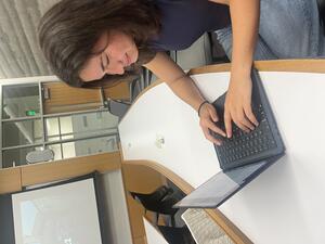 Lily Feldman sitting at a long desk working on a laptop