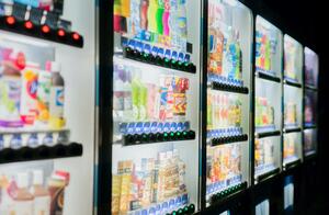 Row of beverage vending machines set against a black background with a focus on the glow of beverage choices available